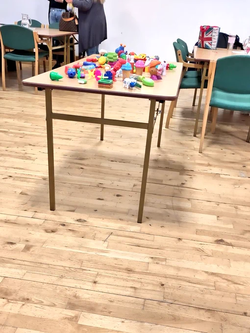 Table with various brightly coloured, bimanual (2 handed) toys scattered on it that work in different ways, e.g. pulling apart, magnetic, and different sizes.