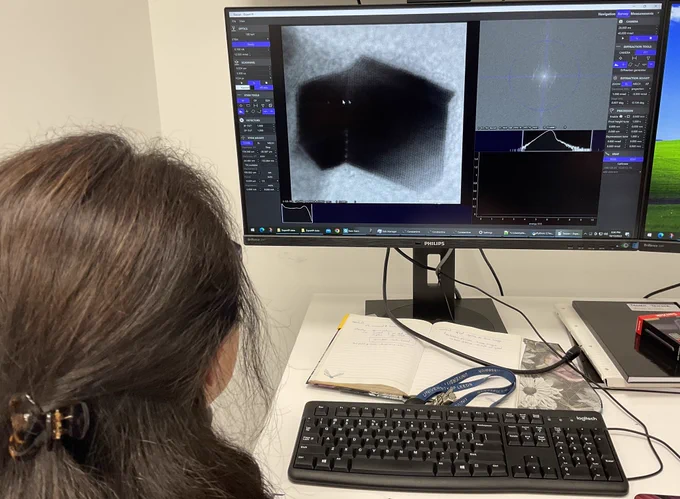 Zabeada sat at a computer which is running the Tescan Tensor, on the screen is a lattice image of a nanoparticle