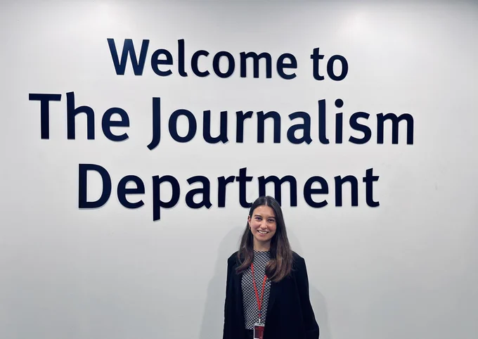 Yara standing in front of a sign reading ‘Welcome to the Journalism Department’