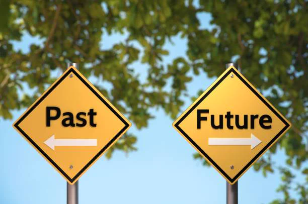 Two yellow road signs are side by side. One says "Past" with backward-pointing arrow, and the other "Future" with arrow pointing forward. 