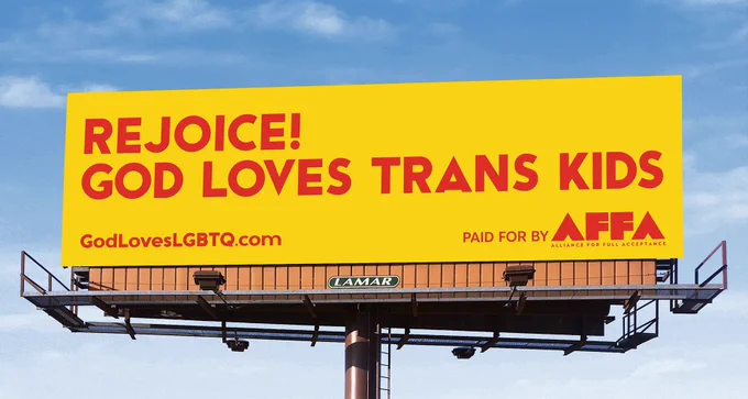A highway billboard reading “Rejoice! God lives trans kids”