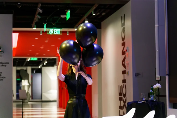 Magician Jeanette Andrews stands holding three black balloons in front of her face. 