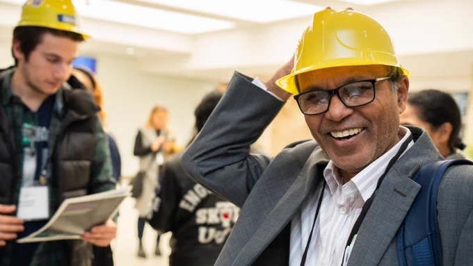 A person wearing a toy yellow hardhat smiles. 