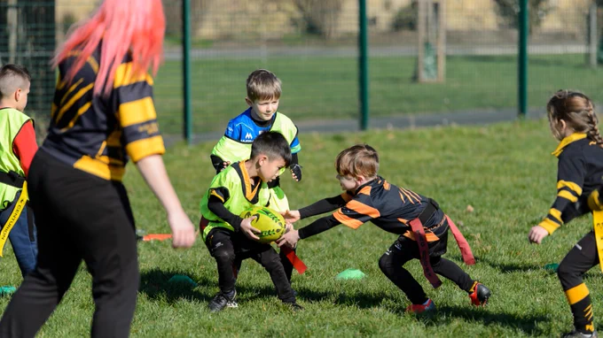 Group of children playing rugby on a grass playing field.