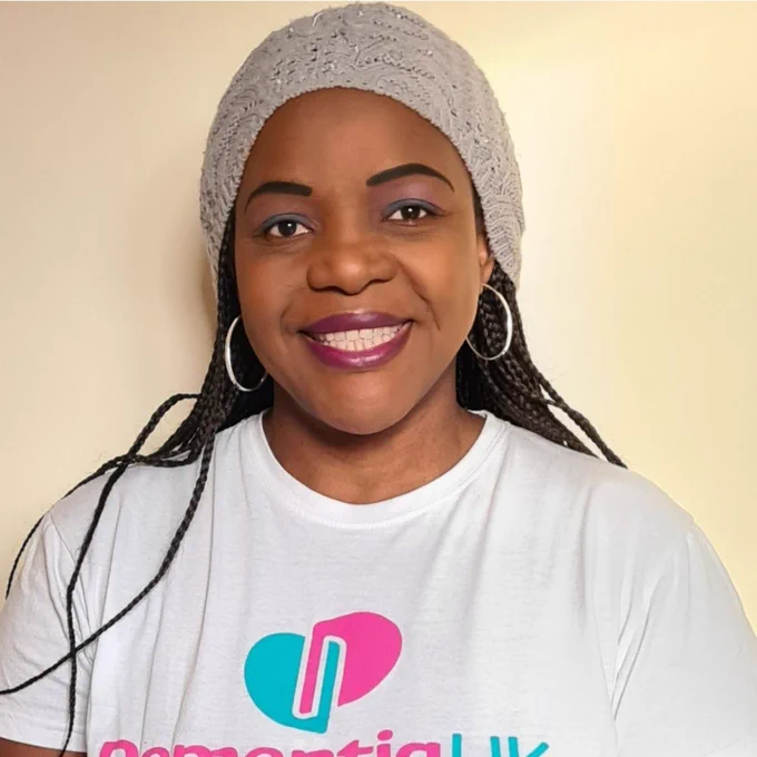 Close up of a woman called Tidziwe smiling. She is wearing a beanie hat wearing a Dementia UK t-shirt.