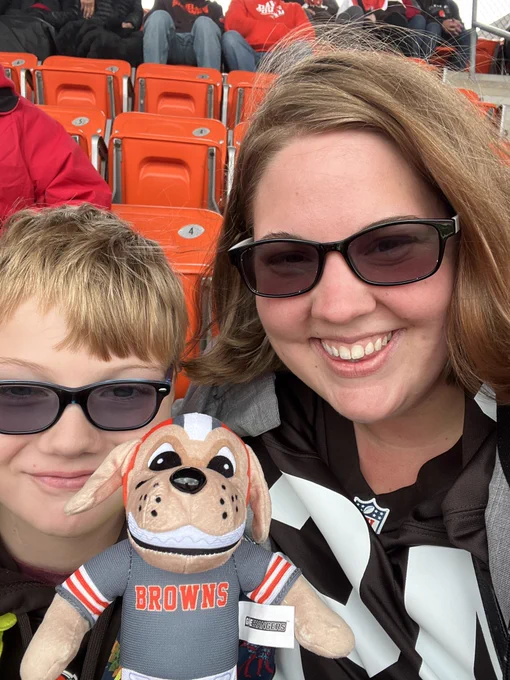 Deb and Ian smiling with the browns stuffed animal mascot between them