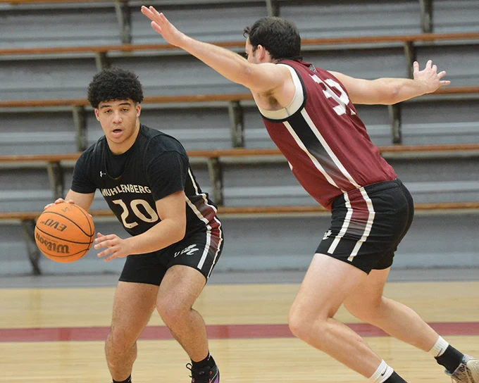 men's basketball player in black jersey guarded by player in red jersey 