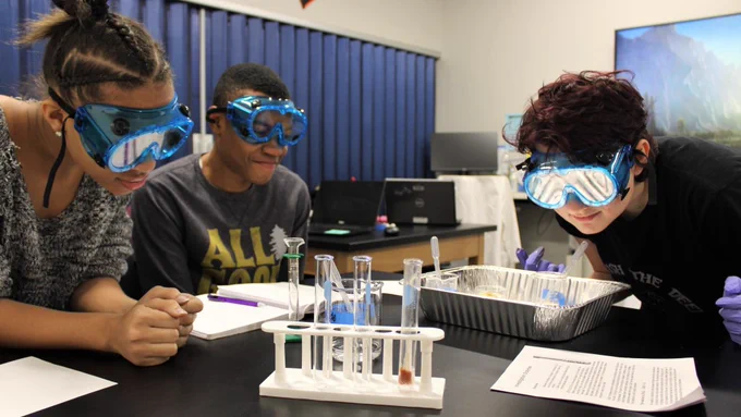 three students wearing goggles in a science lab