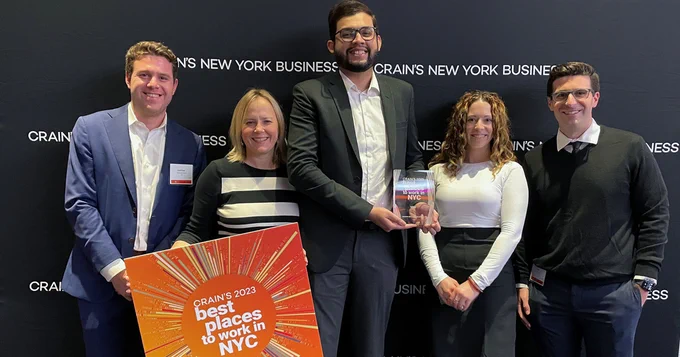 VHBers gather for a photo while holding the award and an orange sign saying, "Crain's 2023 Best Places to Work in NYC."