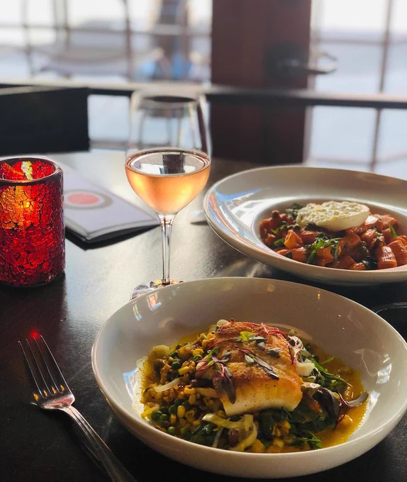 A restaurant table spread with a glass of wine, a candle, and two plates of food.
