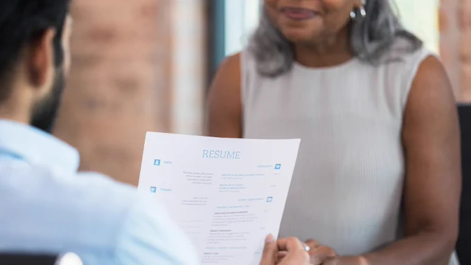 Job seeker holding up a resume facing a smiling recruiter.