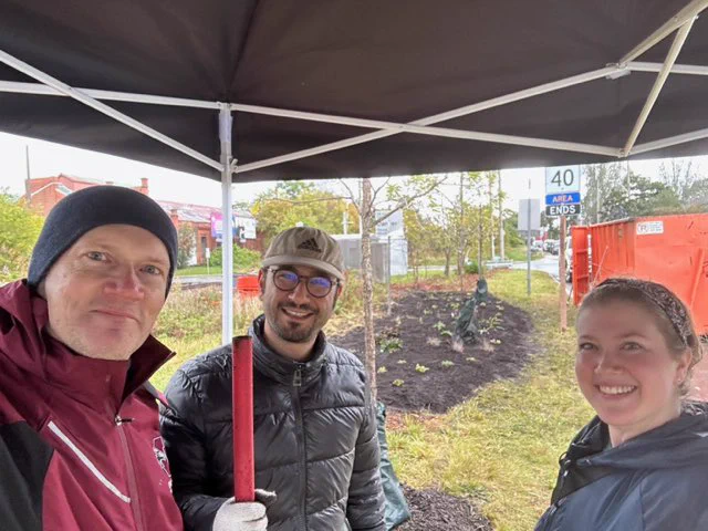 Three people in the rain under a tent at a tree planting event in Hamilton, Ontario, Canada.