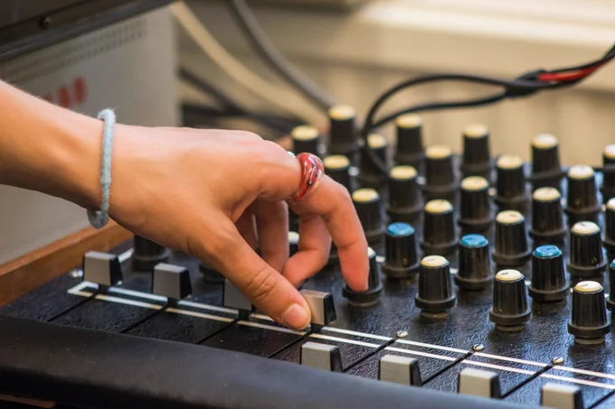 A hand wearing a plastic ring operating a slider on a large mixing desk.