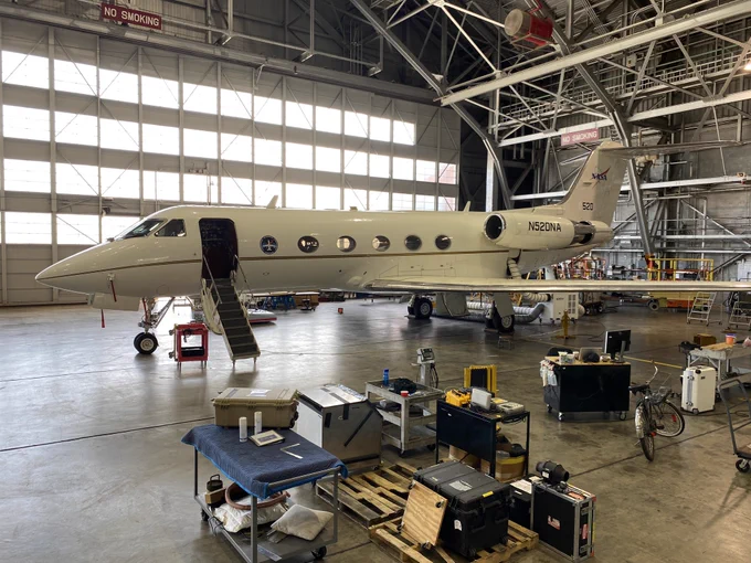 Photo credits: Cecil Garber

Alt text: A small white plane in a hanger. It has six small windows along the side and the NASA logo on the vertical tail wing. There are mutliple carts with toolboxes and cases on them in the hanger.