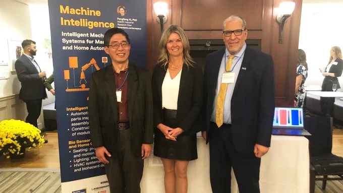 In a room at Queen's Park, professor Fengfeng (Jeff) Xi and TMU president Mohamed Lachemi along with another attendee smile in front of a banner about using machine intelligence for advanced manufacturing and home automation. 