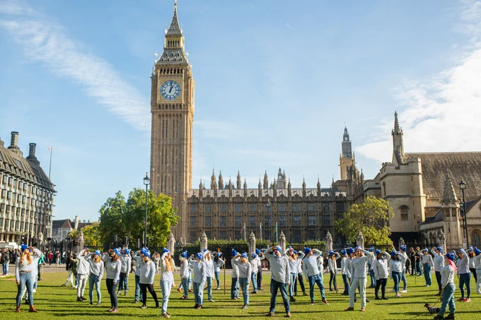 Lots of people in stripey tops and blue bobble hats (like Where's Wally?) standing outside the houses of parliament. They are searching around as though they're looking for something.
