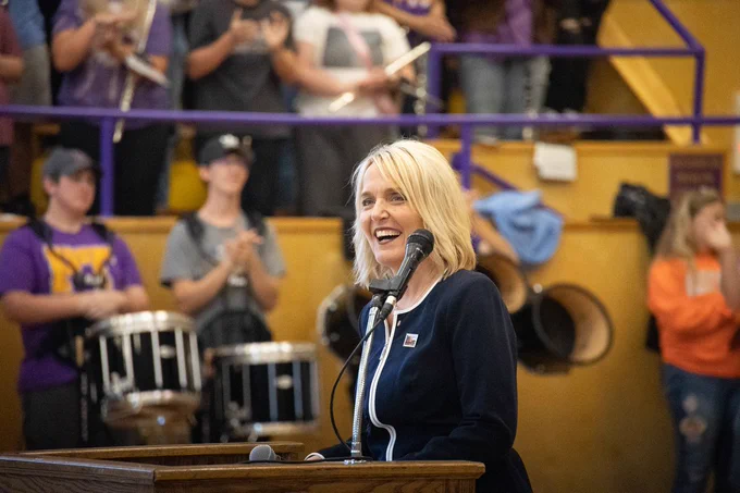 Commissioner of Education Margie Vandeven smiling in a school gym with band students in the background. 