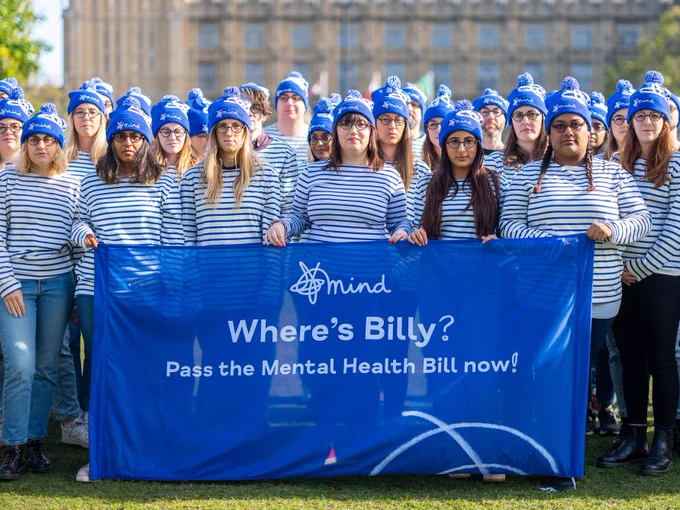 More people in stripey tops and bobble hats. This time they're all looking at the camera and they're holding a banner that says 'Where's Billy? Pass the Mental Health Bill now!'