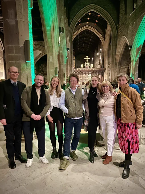 A group of seven people gathered in a cathedral, smiling for a group photo after a conference dinner.