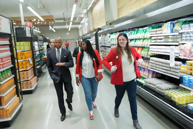 Mayor walks around new target store next to refrigerated dairy and egg section on the right and two other target employees accompanying him