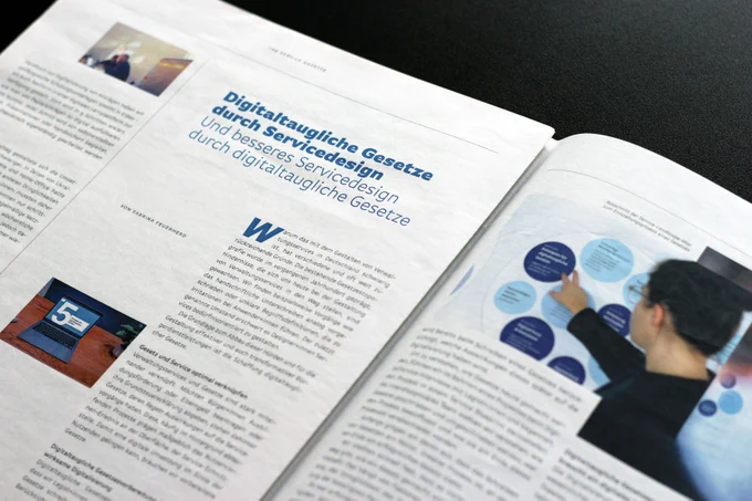 Eine aufgeschlagene Zeitungsseite mit Textspalten, einigen Bildern von Computern und Menschen und einer Überschrift, die sagt: ›Digitaltaugliche Gesetze durch Servicedesign und besseres Servicedesign durch digitaltaugliche Gesetze‹