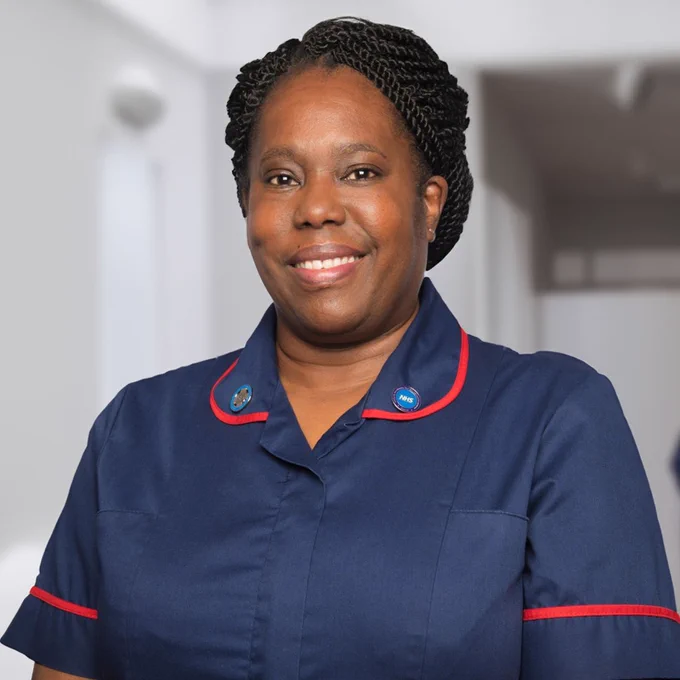 Geraldine is standing and smiling while wearing her NHS uniform. 
