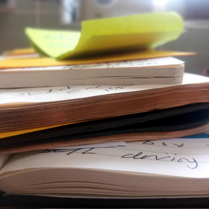 A stack of note books and a yellow post it note on top, seen from the side with page edge visible 