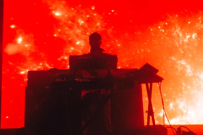 The Comet Is Coming's synth player Danalogue, performs on front of an orange screen at Green Man 2023