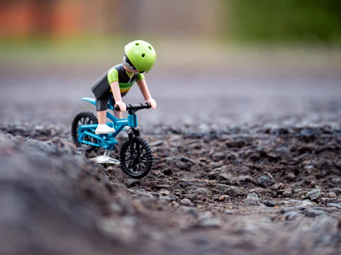 A play mobile figure on a bicycle rides into a large pothole