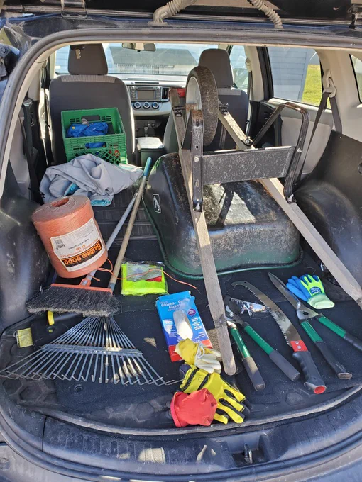 Photo of the inside of an SUV, viewed from the open back door. Back seats have been removed and vehicle floor is piled with a wheel barrow, rake, pruners, gloves and various other yard work equipment.