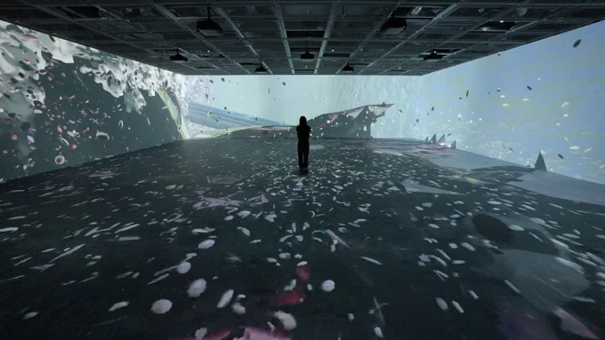 The exhibition space is animated by projections of a fluid carrying microplastics and a human figure is immersed in the experience