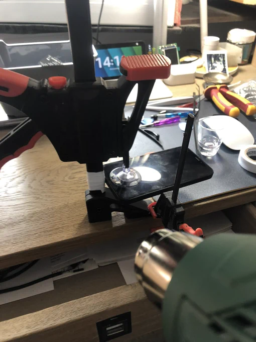 Photo of a repair scenery showing an iPhone 12 Mini between two suction cups in a clamp, with a heat gun directing at it.