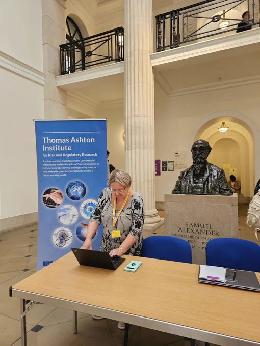 Desk with person at laptop. Behind them is a banner and bust 