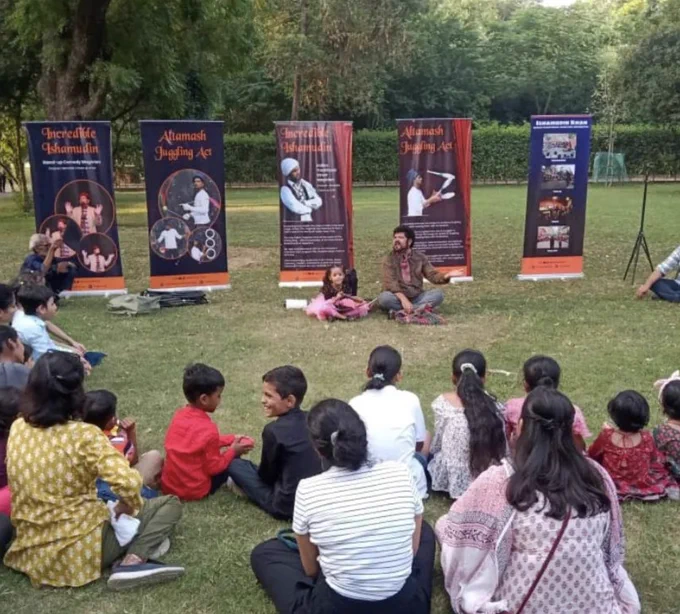 Indian tribal street magician Ishamudin Khan sitting besides a little girl facing a crowd of onlookers during one of his magic shows at Sunder Nursery Park.