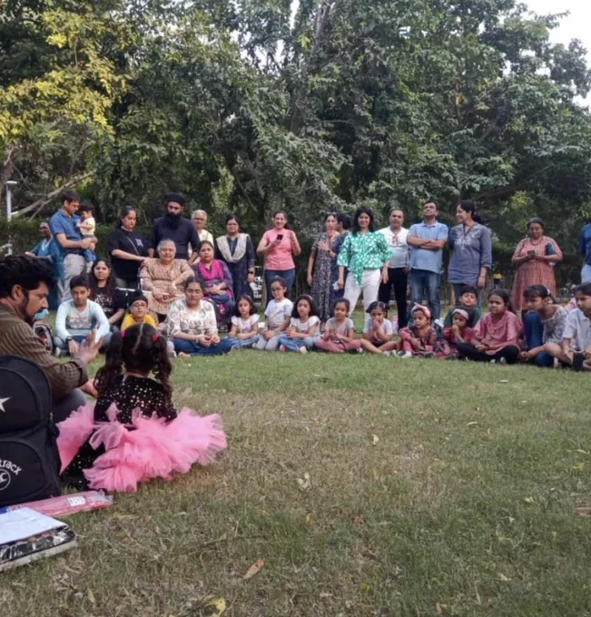 Indian tribal street magician Ishamudin Khan sitting besides a little girl facing a crowd of onlookers during one of his magic shows at Sunder Nursery Park.