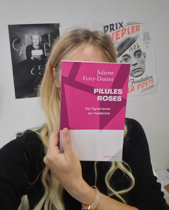 Un selfie où je me cache derrière mon livre : Pilules roses : de l'ignorance en médecine. Stock essais. Le livre est rose vif.
