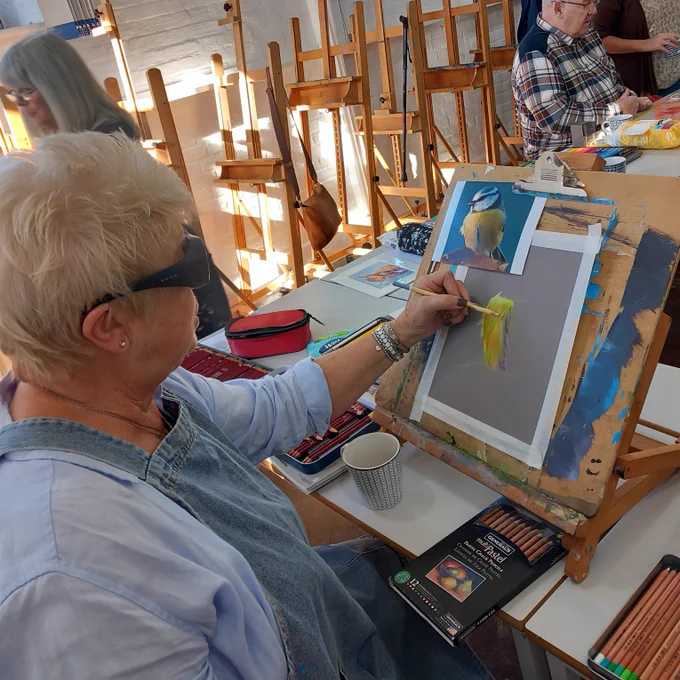 Sue wearing the EnChroma fitover frames over her existing glasses, colouring a picture of a colourful bird during her art class.