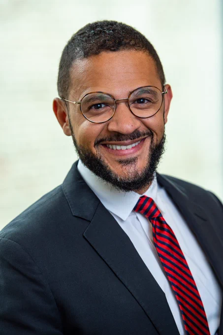 A headshot of new District 2 Multnomah County Commissioner Jesse Beason, wearing a blue suit with a red and black striped tie. 