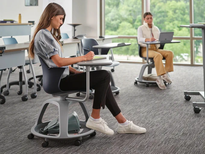 Two college students sit in a classroom in Steelcase Node Chairs that have an attached desk.