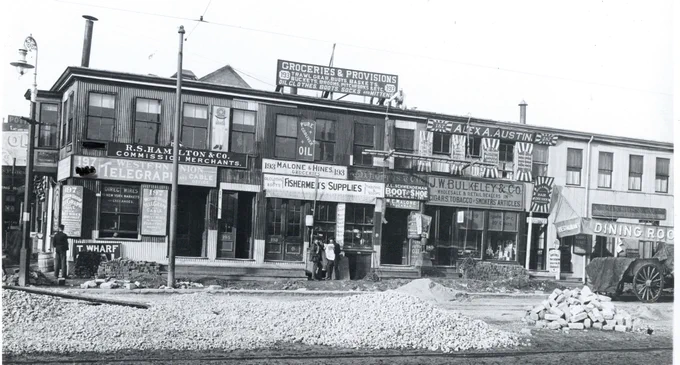 Street scene with stores advertising fishermen's supplies, groceries, laundry, hairdressing, and dining