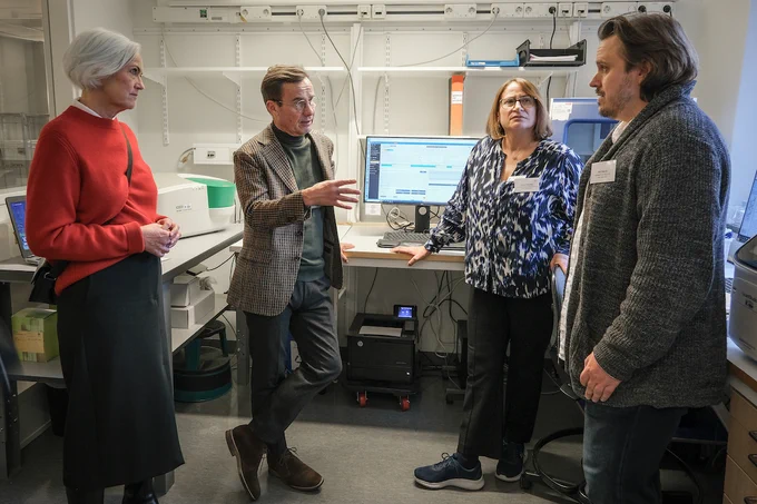 Acko Ankarberg Johansson, Ulf Kristersson, Lucia Cavelier och Per Sikora samtalar framför sekvenseringsinstrument och datorskärm.