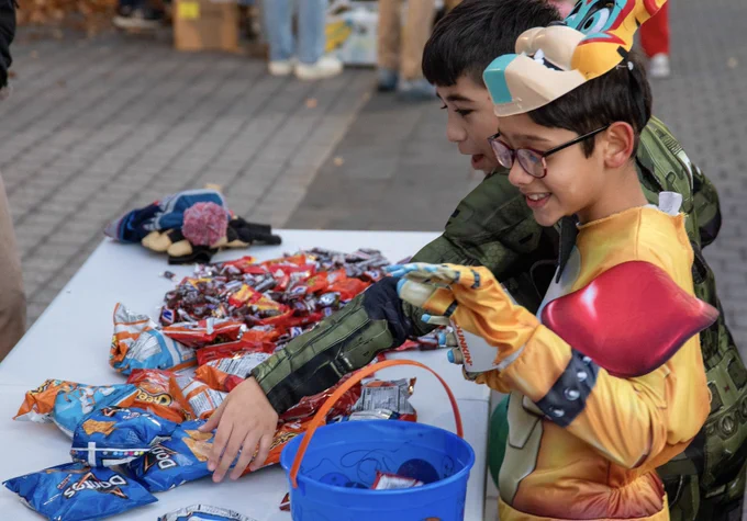 Two trick-or-treaters select some candy and chips from a treat-filled table along Alumni Walk.