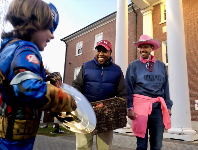 President Garry W. Jenkins and husband Jon Lee smile as they hold a wicker basket of candy as they greet a young boy dressed in a Captain America costume to campus.