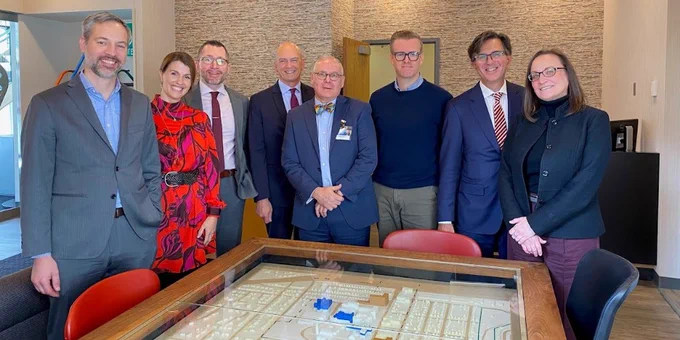 A group of people stand and smile with Commissioner Varilek for a photo in front of a table with a small scale replica. 