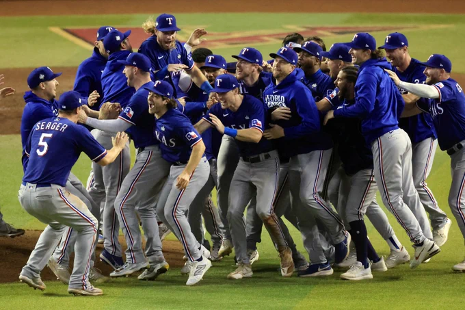 The Rangers mob each other on the field as they celebrate clinching the 2023 World Series. They wear blue Rangers jerseys with gray baseball pants.