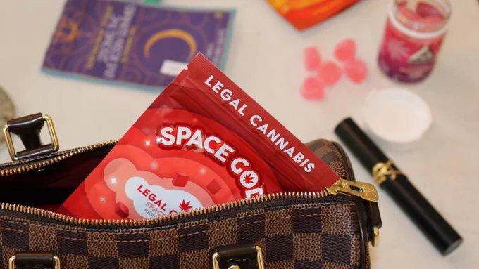 Red plastic packet labelled "legal cannabis" in a handbag on a table with other objects out of focus