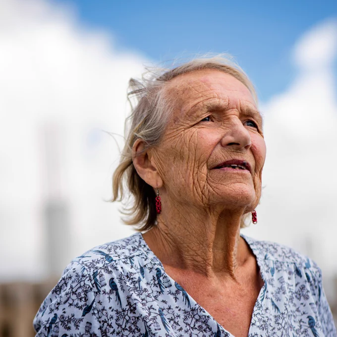 A person stands looking out past the camera into the far distance, as if remembering something, with a cloudy blue sky behind them.