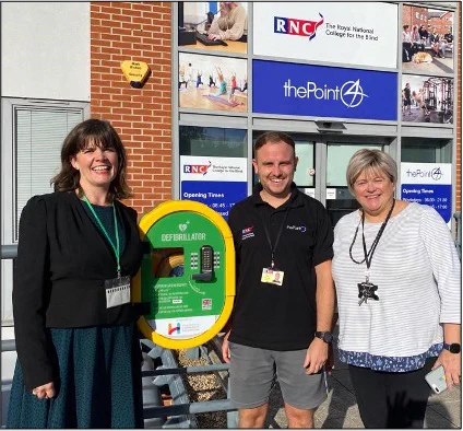 3 people stand with the defibrillator outside of thePoint4 and RNC reception entrance