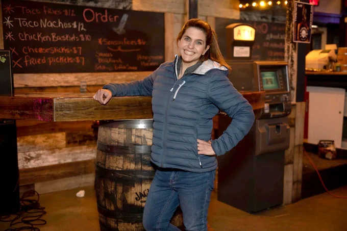Michelle Mary Schaefer standing at a rustic food counter smiling wearing a fluffy winter jacket