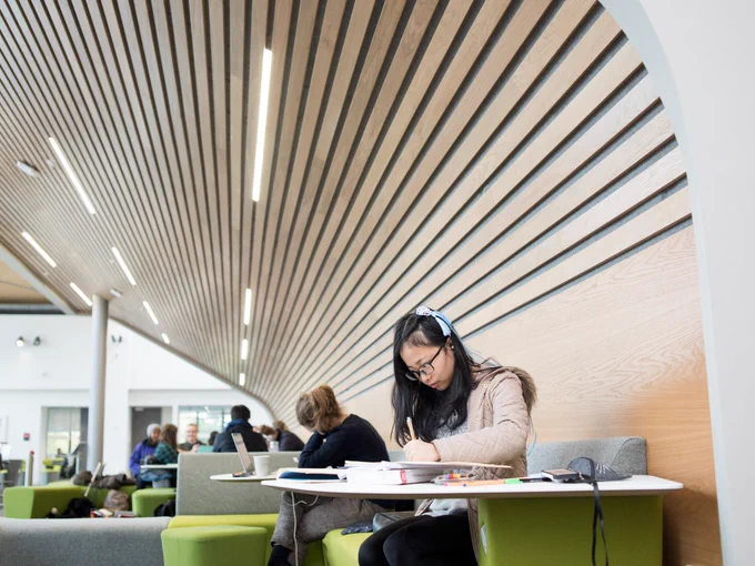 a student studies at a table on the mezzanine floor of the Oculus. They sit, with a pen in hand, making notes.